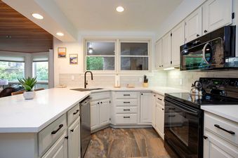 A modern kitchen in Chateau Chamonix CX212 featuring white cabinets, dark tile flooring, and sleek black appliances with a large window above the sink.