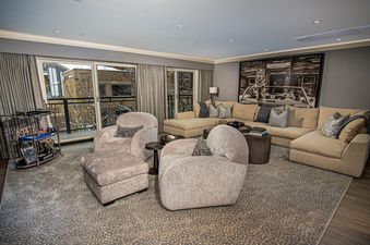 The Clubhouse features a large, comfortable living room with a sectional sofa, two armchairs, and a coffee table. The room is decorated in a contemporary style with a large, framed print of a wolf on the wall. The living room has a modern, cozy feel.