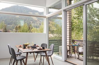 Dining area with a wooden table, grey chairs, and a sliding glass door leading to a balcony with mountain views.