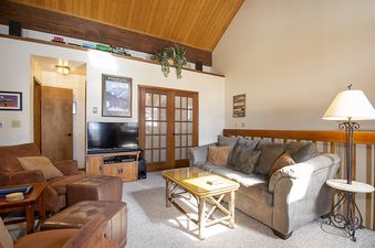 The living area of Kings Crossing Townhome 4 features comfortable seating, a television, and rustic wooden accents under a high vaulted ceiling.