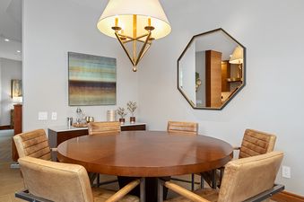 A dining room with a large wooden table surrounded by six leather chairs, a large mirror, and a modern chandelier