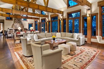 The living area of A Creekside Lodge features large windows, a stone fireplace, and a comfortable sectional sofa.