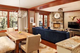 A luxurious and warm open-concept living and dining area inside The Star Two Bedroom Residence, featuring a fireplace, a large blue sectional, and rustic mountain decor.