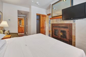 A luxurious bedroom at Mountain Lodge One Bedroom Deluxe Condo with a comfortable bed, fireplace, and flat-screen TV.