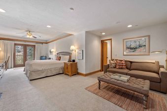 A spacious guest room at The Charter C3305 with a large bed, a comfortable lounge area with a sofa and ottoman, and French doors leading to a balcony.
