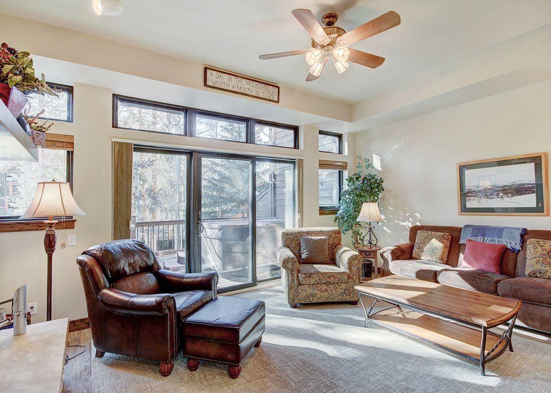 A living room with a couch and chairs facing a large window looking out onto a balcony.