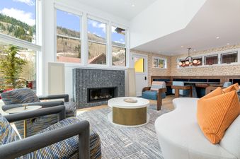 A modern living room with a fireplace, large windows, and a view of a mountain range.