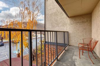 The balcony of Copperbottom 205 features orange wire chairs, a black metal railing, and a view of a birch tree with yellow leaves, a parking lot, and mountains.