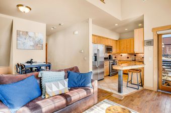 Living room with a leather couch and a kitchen with stainless steel appliances in the background.