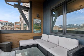 A comfortable outdoor sectional sofa with light gray cushions on the Bear Den's balcony, overlooking snow-capped mountains.