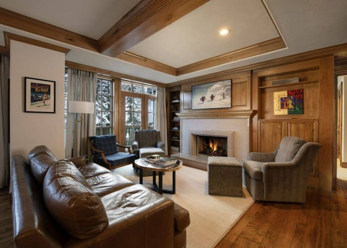 A cozy living room at Chateau Residence 403 features a leather sofa, two armchairs, a fireplace, and large windows with a snowy outdoor view.