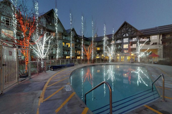 The Aspens on Blackcomb Unit 113 features an illuminated outdoor pool area with glowing trees and a surrounding lodge.