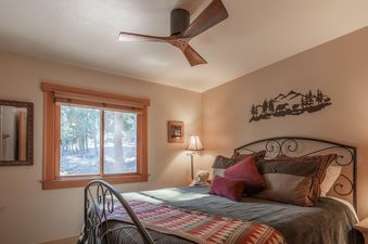 A cozy bedroom at Northstar Ski View Condo with a large window overlooking trees, a comfortable bed, and unique rustic decor.