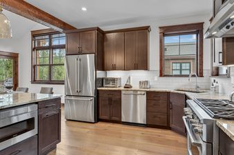 A modern kitchen at Cherrybrook Chalet with dark wood cabinets, stainless steel appliances, granite countertops, and a white subway tile backsplash, featuring large windows overlooking a lush outdoor setting.