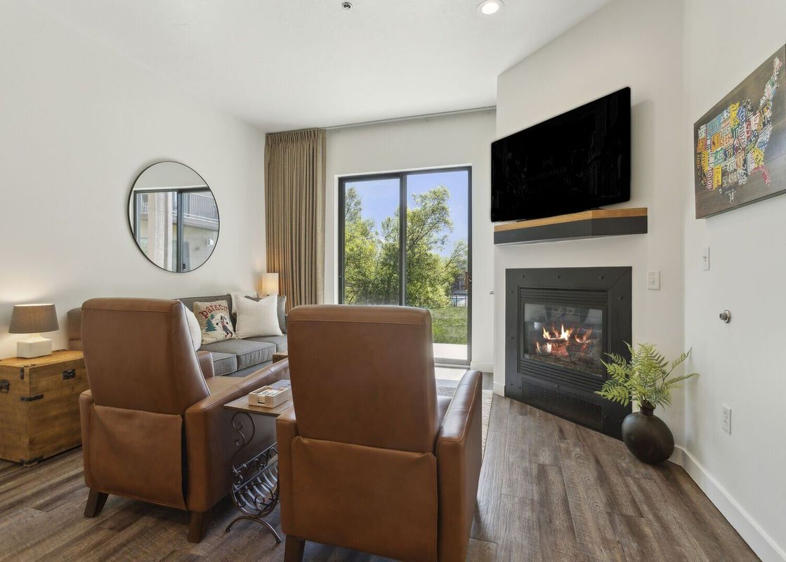 The living room at The Mason 1052 features a cozy fireplace, comfortable seating, and a large window offering a view of lush greenery.