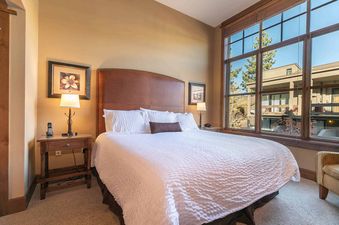A bedroom with a king-sized bed, a brown leather headboard, and a large window with a view of a mountainside.