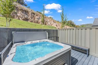 A private hot tub with bubbling blue water is set on a secluded outdoor deck at Frostwood Links, surrounded by a privacy fence and a natural hillside under a clear blue sky.