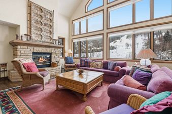 A spacious and elegantly furnished living room at Highlands Slopeside 502, featuring a warm fireplace, plush sofas, and floor-to-ceiling windows with stunning views of snow-covered mountains.