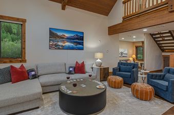 The living area at Royal Retreat features a large sectional sofa, a coffee table with board games, and two blue armchairs, with a large TV on the wall and wooden beams on the ceiling.