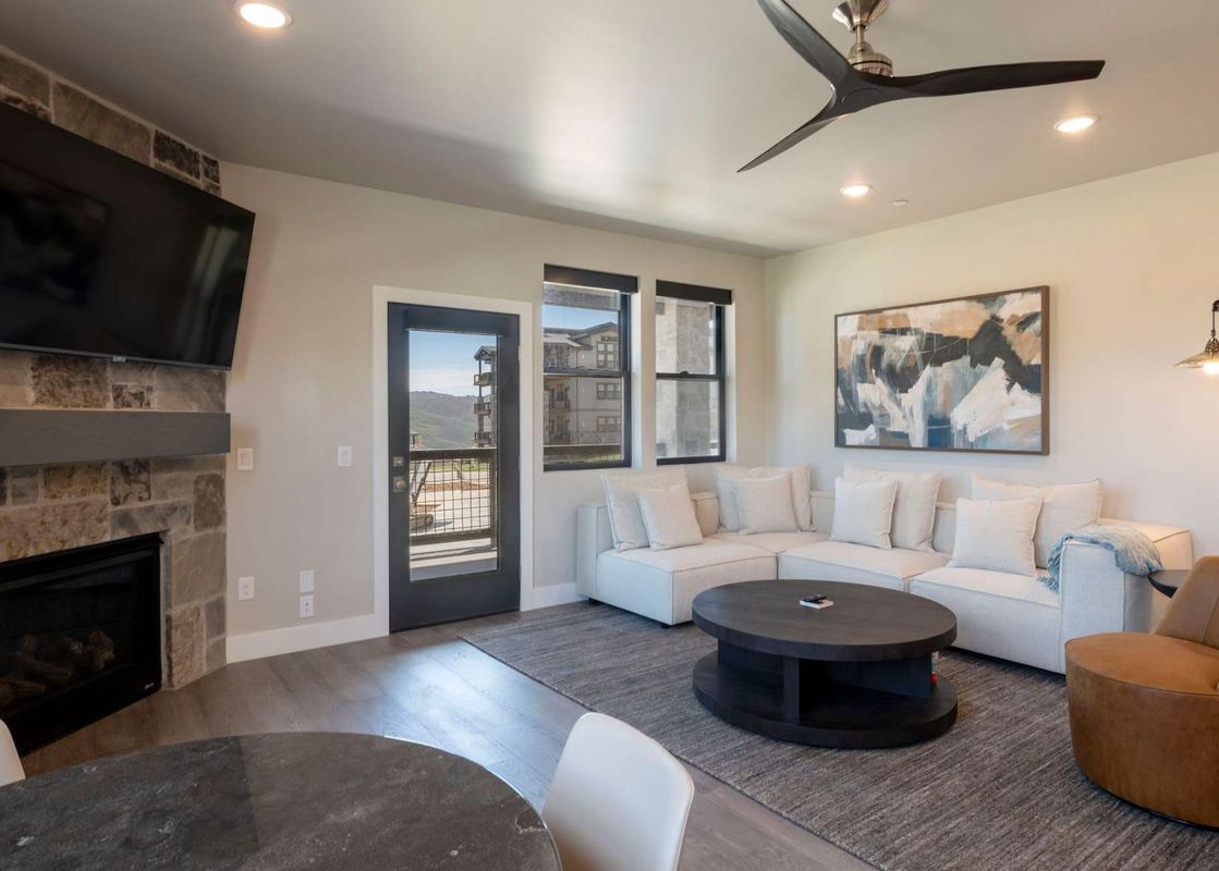 A spacious and inviting living room at the Retreat at Jordanelle features a comfortable white sofa, a large fireplace, and a door leading to a balcony with mountain views.