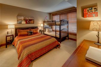 A bedroom with a striped comforter on the bed, a bunk bed, and two lamps on nightstands.