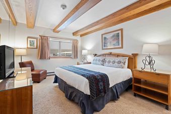 Cozy bedroom at the Lodge at Lionshead 270A with a large bed, wooden ceiling beams, and a television.