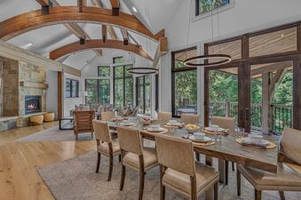 Open-plan dining and living area in Moose Meadows Reserve featuring a wooden table, fireplace, and vaulted beamed ceiling.