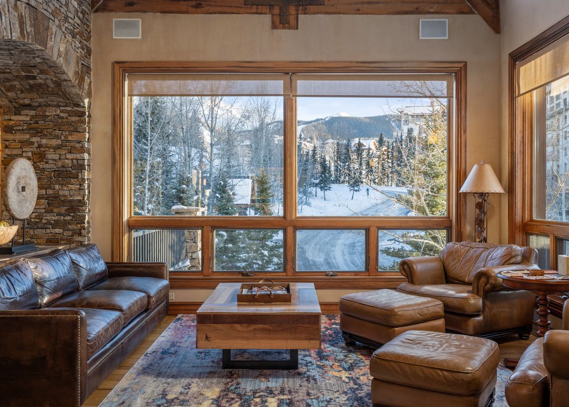 A cozy living room with leather furniture and large windows looking out onto a snow-covered mountain landscape.