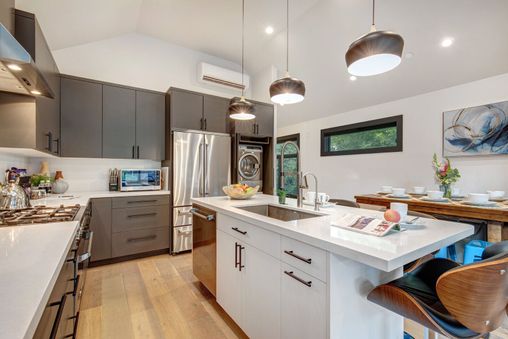 A modern kitchen with white cabinets and a stainless steel refrigerator, a black barstool, and a white countertop with a magazine on it.