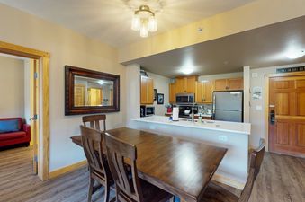 A dining room with a wooden table and chairs, and a kitchen in the background.