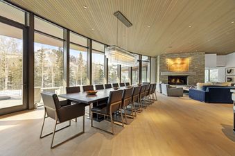 The grand dining area of Alpine Opus features a long dining table with black chairs, set against a stunning backdrop of snow-dusted mountains visible through large windows.