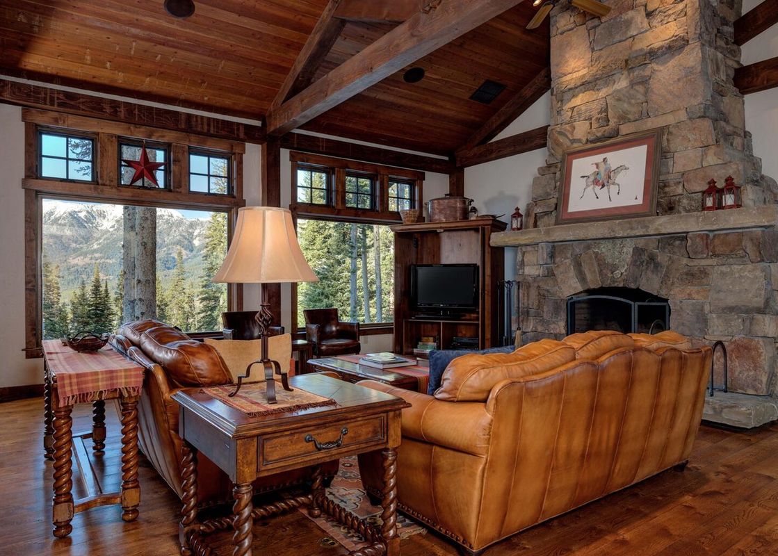 A living room in Moonlight Basin 20 Peaks View with a large stone fireplace with a hearth and a wood mantle, and leather sofas in front of the fireplace.