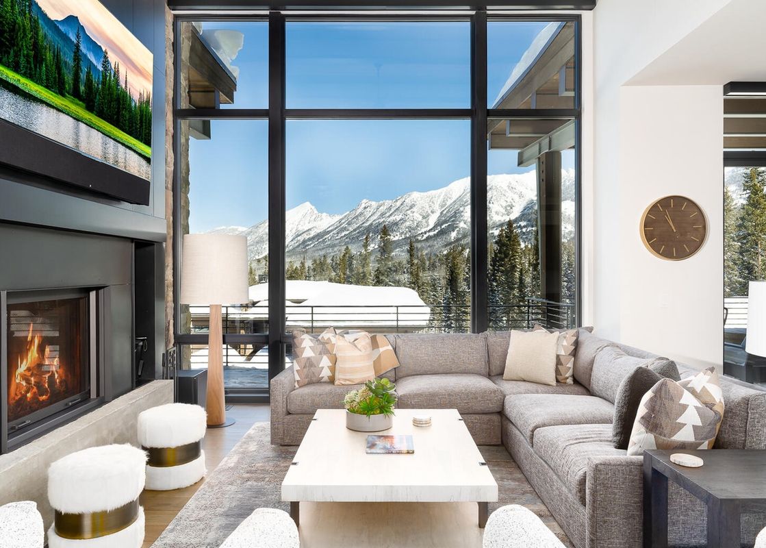 A living room with a sectional sofa and a large window overlooking a snowy mountain range.