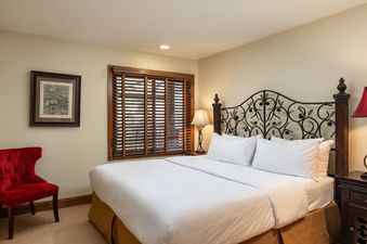A cozy bedroom in Montaneros 418 featuring a bed with a wrought iron headboard, white linens, and a red armchair.