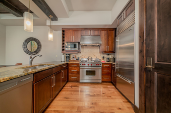 The modern, stainless steel kitchen in Lumiere One Bedroom Deluxe Residence features a sleek, stainless-steel stovetop, oven, and range hood. It's equipped with a dishwasher and granite countertops.