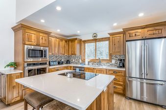 Kitchen with stainless steel appliances, wooden cabinets, a white countertop, and a window with a view of a snowy forest.