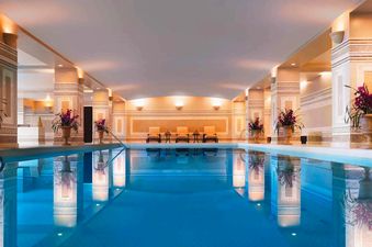 An expansive indoor swimming pool at the Montage Deer Valley King Room Resort View is illuminated by elegant wall sconces and features lush potted plants.