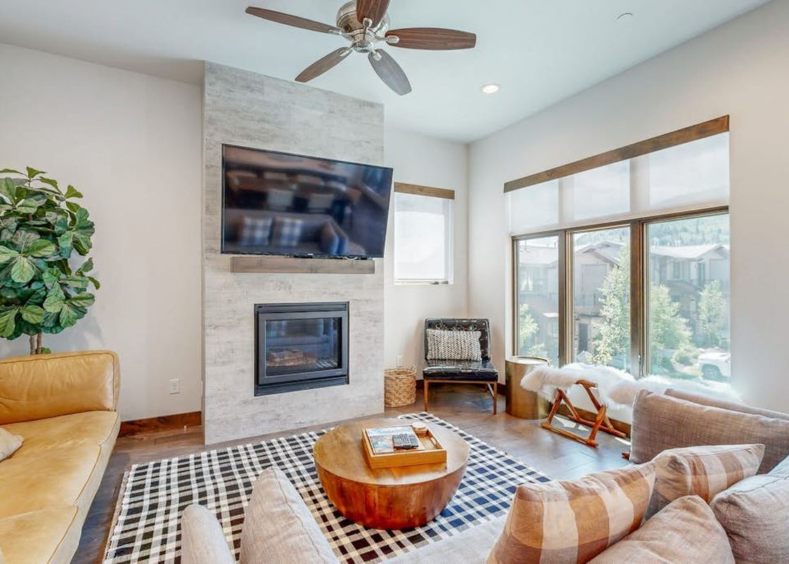 A bright and spacious living room in Modern Blackstone Paradise 2A featuring a fireplace, a flat-screen TV, comfortable sofas, and large windows with an outdoor view.