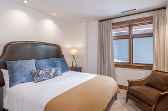 A well-appointed bedroom with a king-sized bed, dark leather headboard, blue pillows, and a window with drapes.