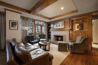 A cozy living room at Chateau Residence 403 features a leather sofa, two armchairs, a fireplace, and large windows with a snowy outdoor view.