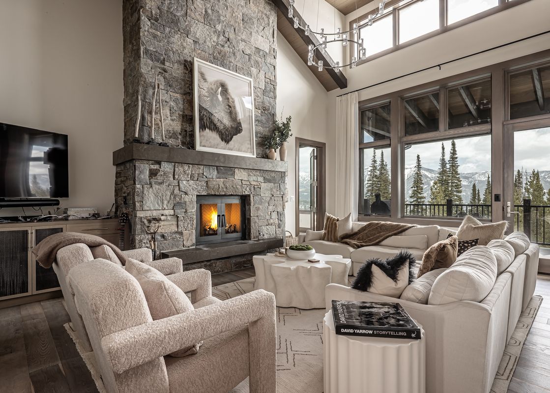 A spacious living room at Inspiration Point Townhome 4C features a stone fireplace, cream-colored seating, and large windows offering panoramic mountain and forest views.