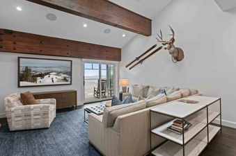A living room in Stag Lodge 11 4BR with comfortable seating, decorative wooden beams, and a view of snow-covered mountains from the balcony.