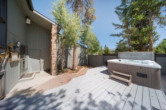 An outdoor view of the Jabberwocky Home's grey wooden deck with a hot tub, surrounded by trees.