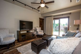 A cozy living room in Baker Loft 203 with a large TV, comfortable seating, and a balcony with an outdoor view.