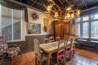 The dining area in Shirana 1 and 7 features a rustic wooden table and chairs, illuminated by an antler chandelier.