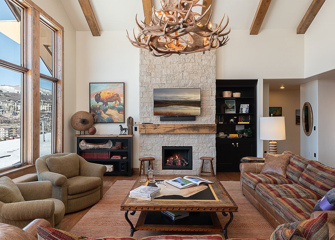 The stunning great room in Edgemont 2803 Nightfall Ridge features a stone fireplace, cozy seating, and expansive windows.