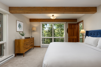 A bedroom with a king-sized bed, a wooden dresser, and a window with a view of trees.