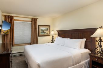 A primary bedroom in Montaneros 306 with a king-sized bed, a flat-screen TV, and a window with blinds and curtains.