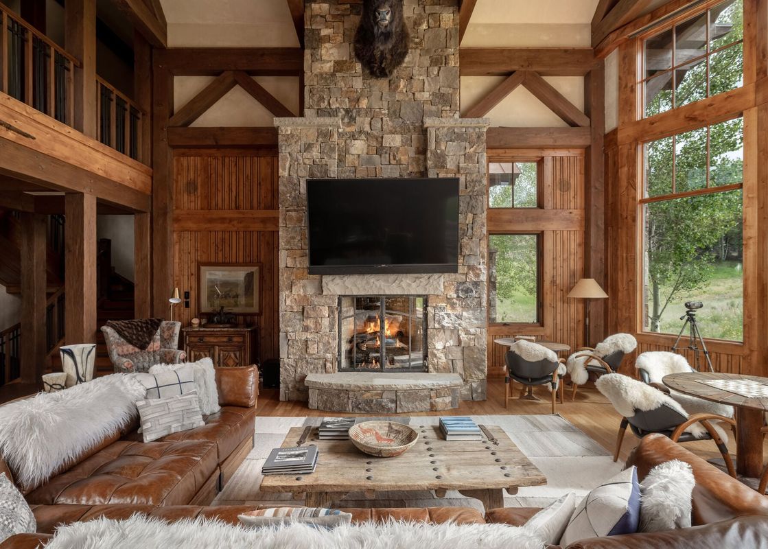 The luxurious great room of Hord Mountain Retreat with a floor-to-ceiling stone fireplace and large windows.