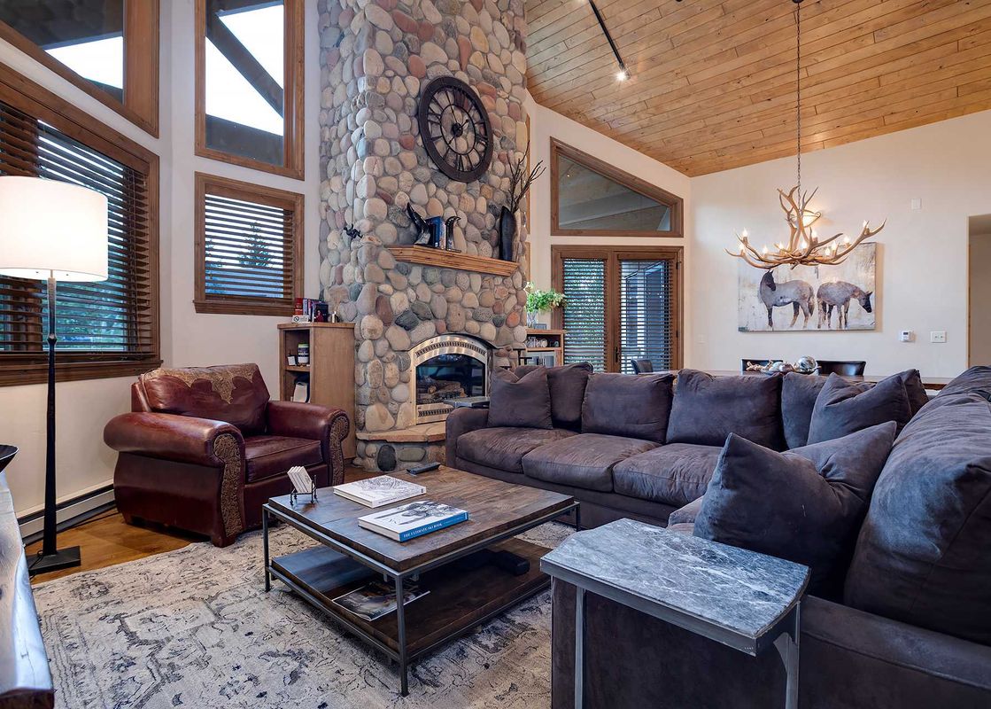 A cozy living room in Chateau Chamonix CX342 with a large stone fireplace, gray sectional sofa, and rustic wood finishes.